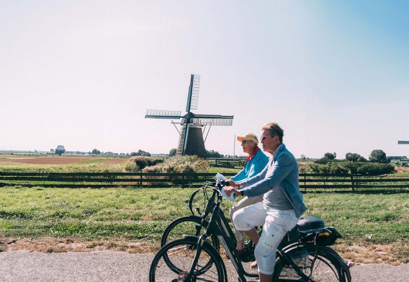 2 oudere mensen fietsen door Ten Boer langs het landschap en een molen.