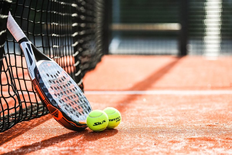 Een padelracket met twee tennisballen en een net